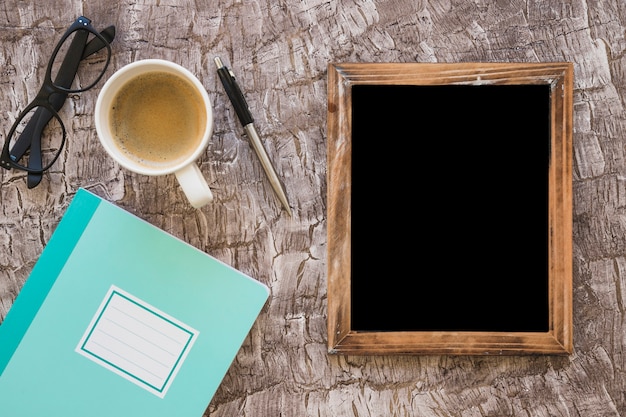 Cuaderno; taza de café; los anteojos; pluma y pizarra en blanco sobre fondo texturizado