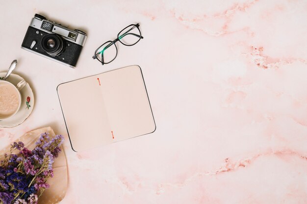 Cuaderno con taza de café, cámara y vasos en mesa