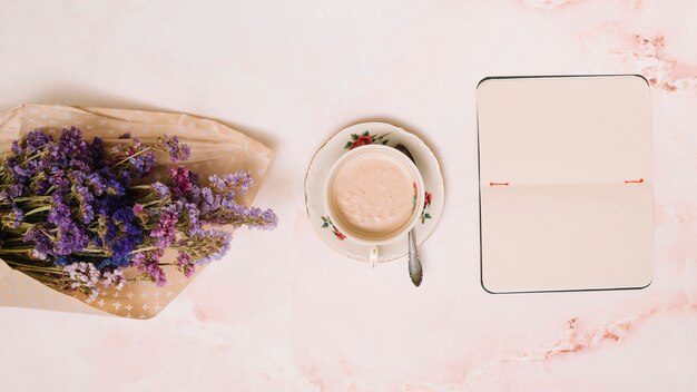 Cuaderno con taza de café y ramo de flores en la mesa