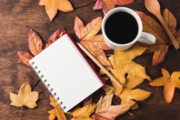 Cuaderno y taza de café sobre fondo de hojas de otoño