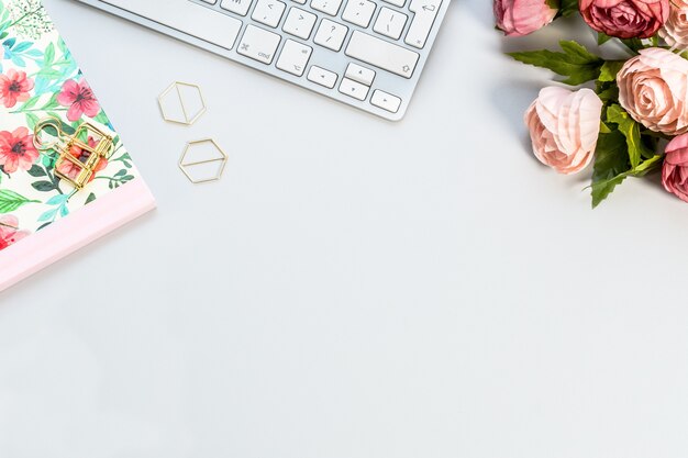 Cuaderno, un teclado blanco y rosas rosadas sobre una superficie blanca