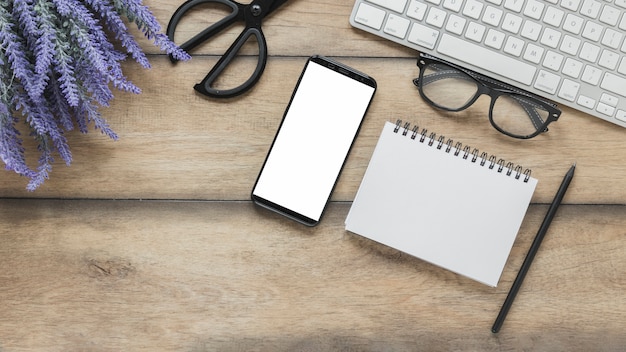 Cuaderno y teléfono inteligente cerca de flores de lavanda y teclado