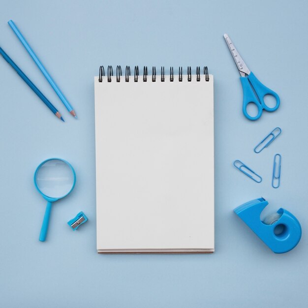 cuaderno con tijeras sacapuntas de lápiz de lupa sobre fondo azul claro