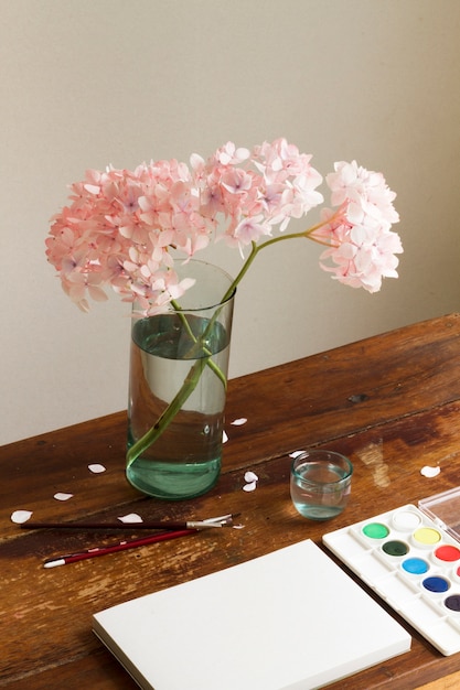 Cuaderno vacío con acuarela y flores en un jarrón en el espacio de trabajo de arte