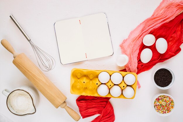 Cuaderno vacío cerca de ingredientes de cocina y herramientas