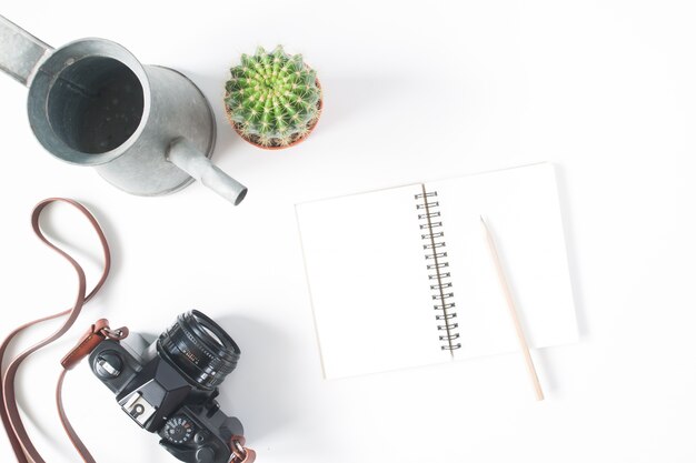 Cuaderno vacío, lápiz, cámara de película, olla de cactus con riego, vista superior, tumbado, aislado en fondo blanco