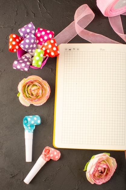 Un cuaderno de la vista superior y flores en el color oscuro de la planta de la flor del escritorio