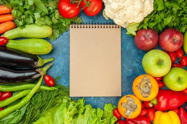 Cuaderno de vista superior con frutas y verduras sobre fondo azul.