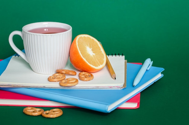 Cuadernos una taza de té y una naranja en un espacio de copia de fondo verde
