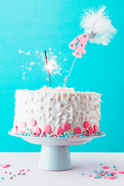 Cuarto pastel de cumpleaños con una bengala encendida sobre una superficie blanca.