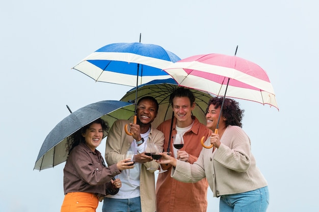 Cuatro amigos bebiendo vino y parados bajo sombrillas durante una fiesta al aire libre