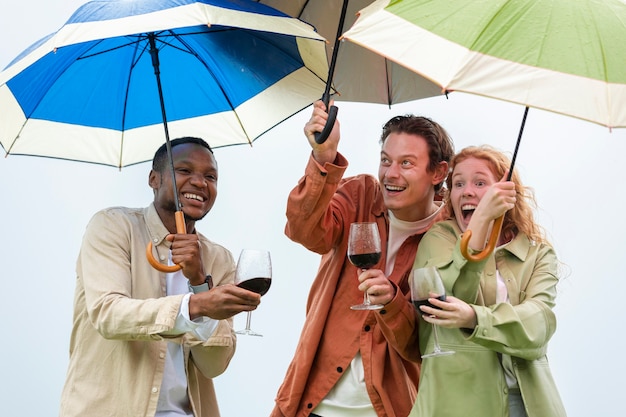 Cuatro amigos bebiendo vino y parados bajo sombrillas durante una fiesta al aire libre