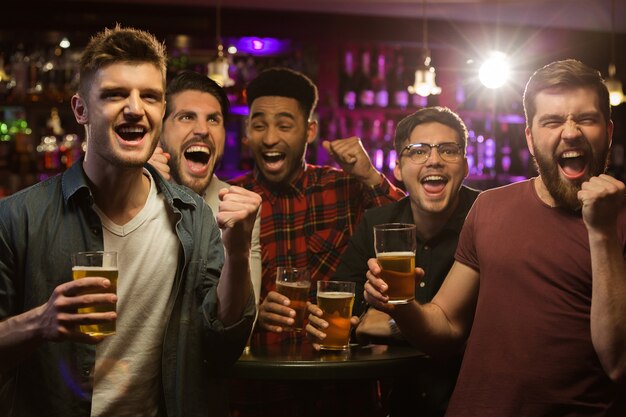 Cuatro hombres felices sosteniendo jarras de cerveza y gesticulando