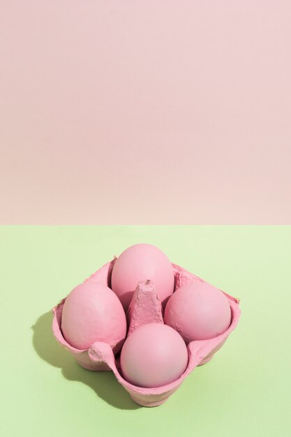 Cuatro huevos de Pascua rosados en pequeño estante en mesa verde