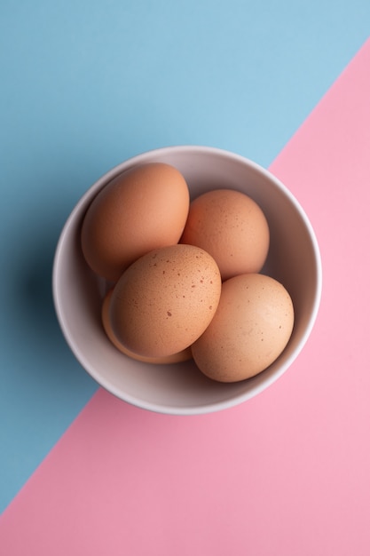 Cuatro huevos en un recipiente sobre una superficie azul y rosa.