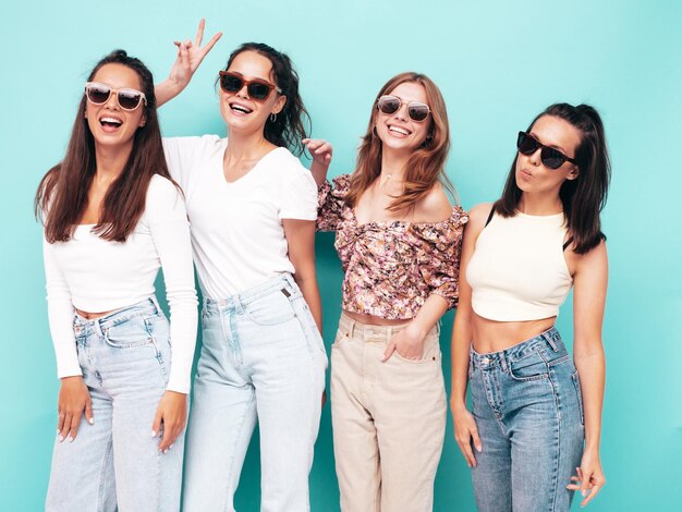 Cuatro jóvenes hermosas mujeres hipster morena sonriente en ropa de verano de moda Mujeres sexy despreocupadas posando junto a la pared azul Modelos positivos divirtiéndose Alegre y feliz En gafas de sol