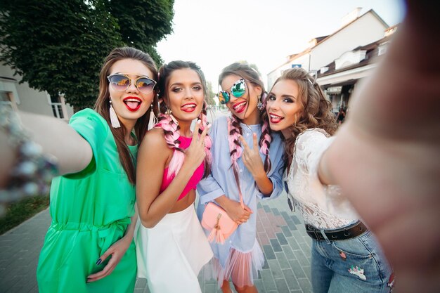 Cuatro mejores amigas de moda y hermosas con anteojos, posando para las redes sociales, el estilo de vida, pasar el tiempo divirtiéndose. Mujeres con gafas de sol después de ir de compras y al salón de belleza.