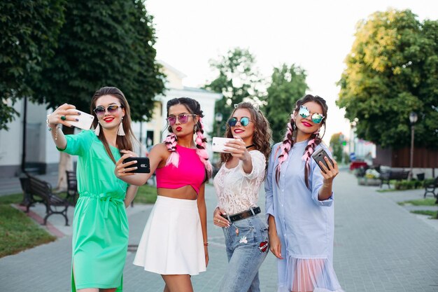 Cuatro mejores amigas a la moda y hermosas con gafas, cada una posando haciendo selfies para las redes sociales, diviértete. Mujeres con gafas de sol después de ir de compras y al salón de belleza.