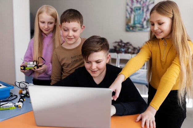 Cuatro niños usando una computadora portátil y piezas electrónicas para construir un robot