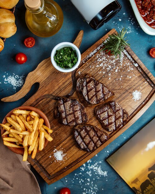 Cuatro pequeños trozos de carne servidos con papas fritas y hierbas picadas