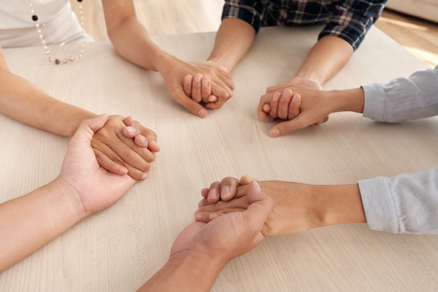 Cuatro personas irreconocibles sentados alrededor de la mesa y tomados de la mano en el medio