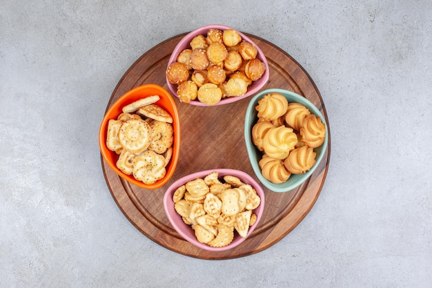 Foto gratuita cuatro tazones de galletas y chips de galleta sobre tabla de madera sobre superficie de mármol.