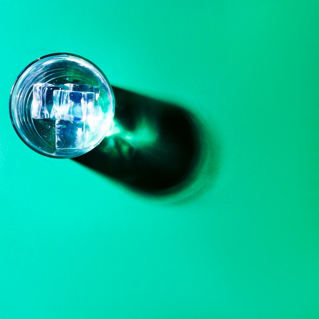 Cubitos de hielo en vaso de agua con sombra sobre fondo verde