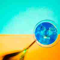 Foto gratuita cubitos de hielo en el vaso de martini azul sobre fondo turquesa y amarillo