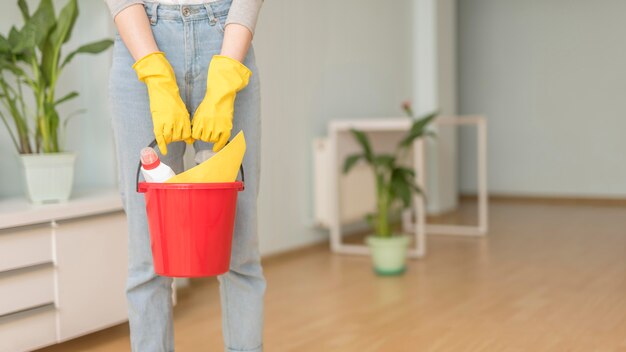 Cubo con artículos de limpieza sostenidos por una mujer con guantes