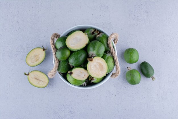 Cubo blanco lleno de feijoas frescas sobre fondo de mármol. Foto de alta calidad