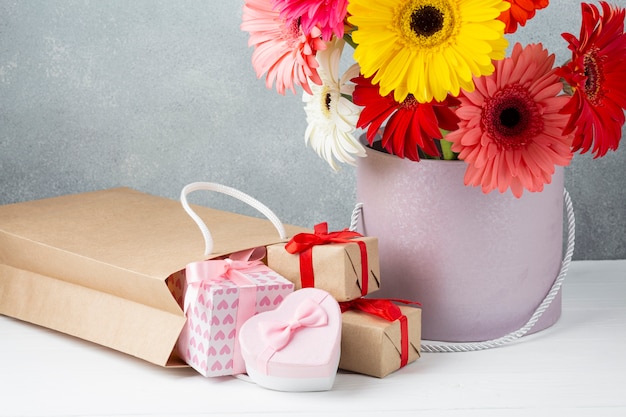 Cubo con flores de gerbera y papeles y cajas de regalo.