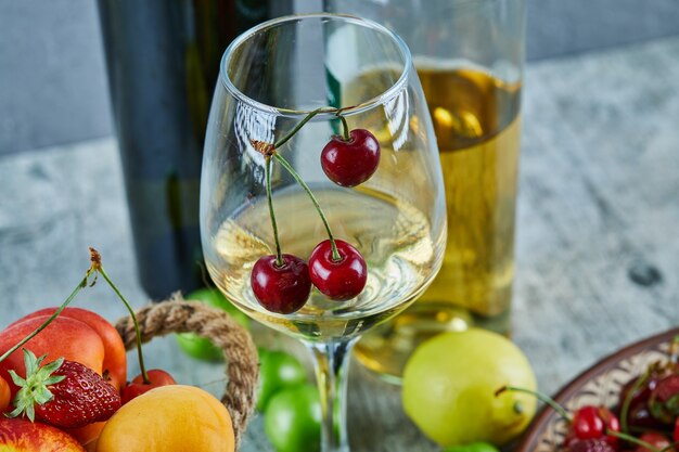 Cubo de frutas de verano, limón y una copa de vino blanco sobre la superficie de mármol