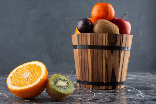 Cubo de madera lleno de frutas frescas sobre la superficie de mármol.