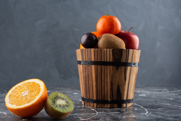 Cubo de madera lleno de frutas frescas sobre la superficie de mármol.