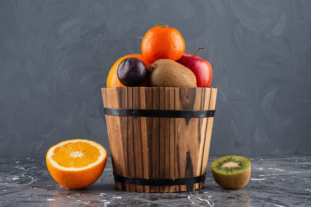 Cubo de madera lleno de frutas frescas sobre la superficie de mármol.