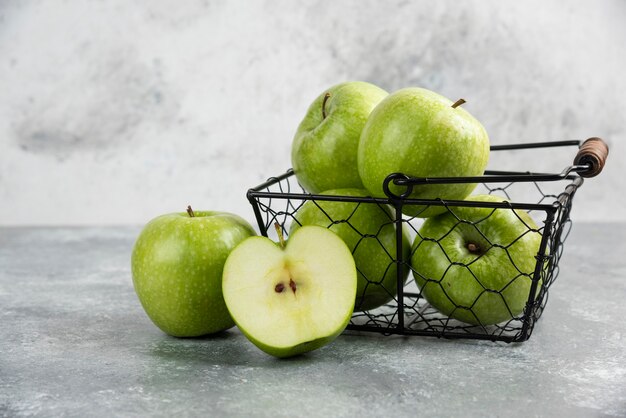 Cubo de metal de manzanas verdes frescas en la mesa de mármol.