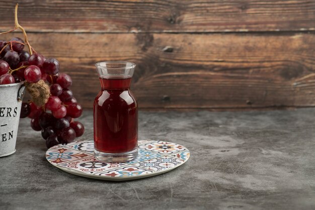 Cubo de metal de uvas rojas frescas y vaso de jugo en la mesa de mármol.