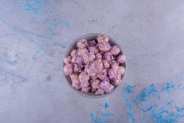 Cubo pequeño lleno de dulces de palomitas de maíz junto a ramas decorativas sobre fondo de mármol. Foto de alta calidad