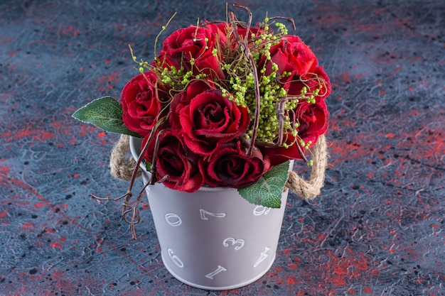 Un cubo con un ramo de hermosas rosas rojas sobre fondo de mármol.