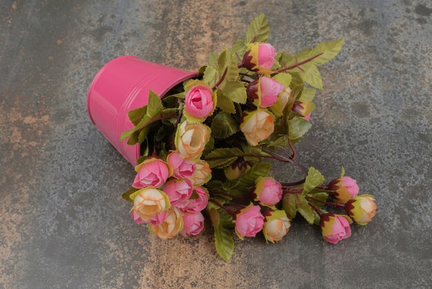 Un cubo rosa con ramo de flores sobre la superficie de mármol.