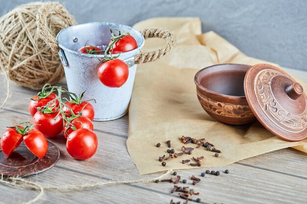 Cubo de tomates y tomate medio cortado en mesa de madera con recipiente vacío