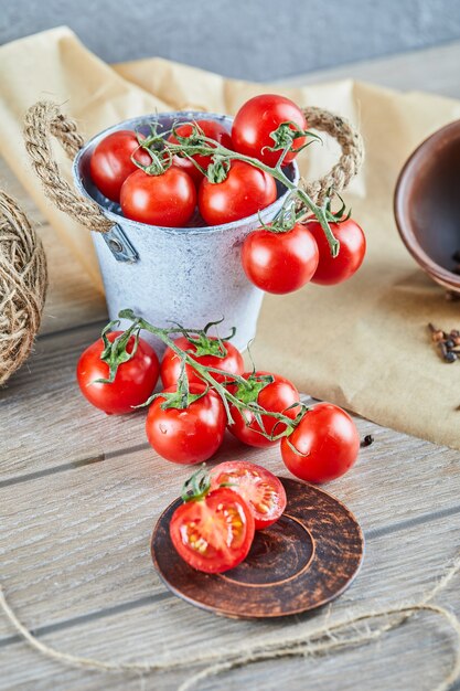 Cubo de tomates y tomate medio cortado en mesa de madera.