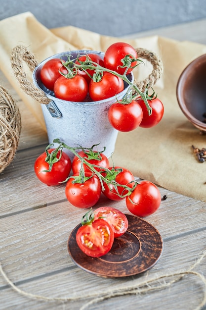 Cubo de tomates y tomate medio cortado en mesa de madera.