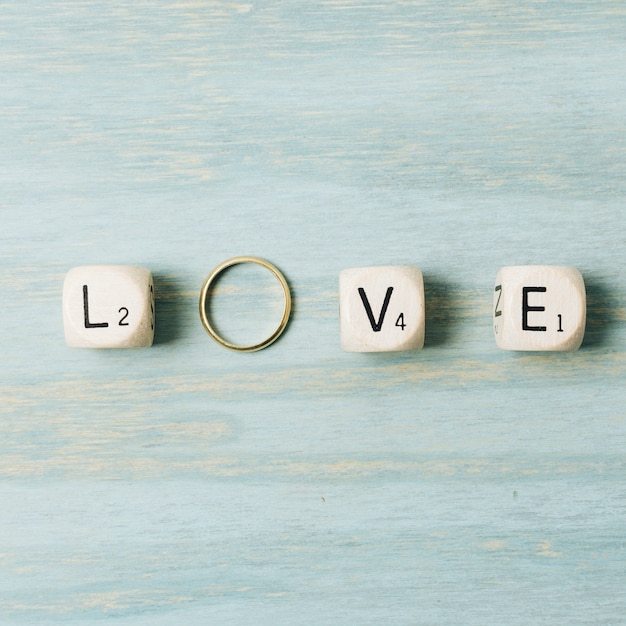 Cubos de la carta de amor con el anillo de bodas de oro sobre fondo de textura de madera