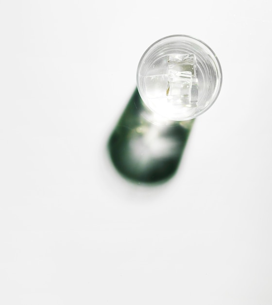 Cubos de hielo en vaso de agua con sombra brillante sobre fondo blanco