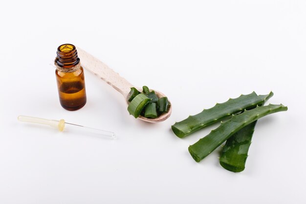 Cuchara de madera con aloe se encuentra en una mesa blanca con una botella de aceite