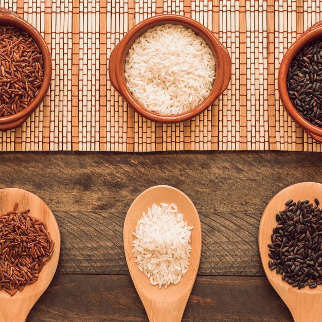 Cuchara de madera y cuenco de granos de arroz en la mesa de madera