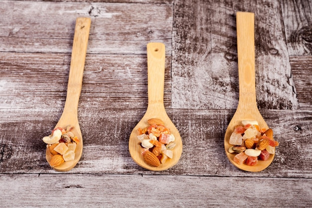 Cuchara de madera con diferentes tipos saludables de nueces y dulces sobre fondo de madera en foto de estudio