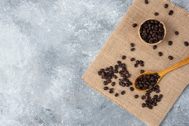 Cuchara de madera llena de granos de café tostados sobre arpillera.