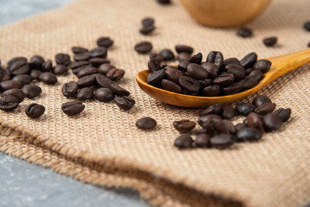 Cuchara de madera llena de granos de café tostados sobre arpillera.